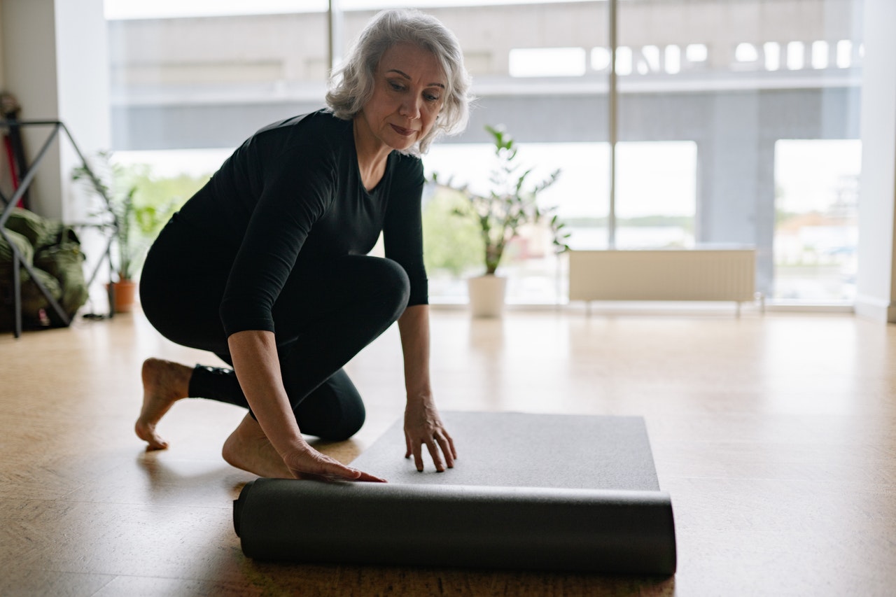 Ćwiczenia dla seniorów - kobieta rozkłada matę do jogi