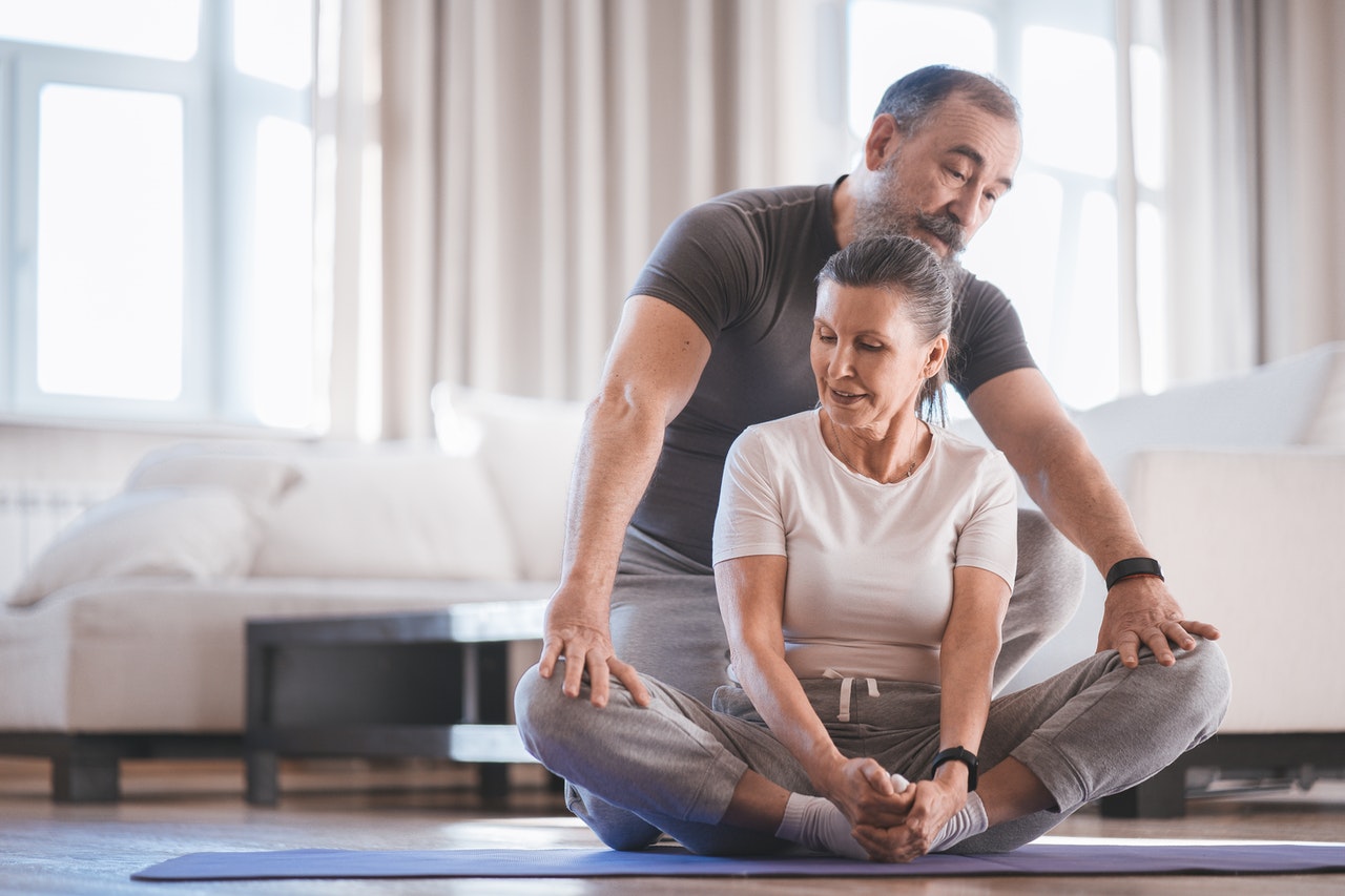 ćwiczenia dla seniorów na kręgosłup - mężczyzna pomaga kobiecie ćwiczyć jogę